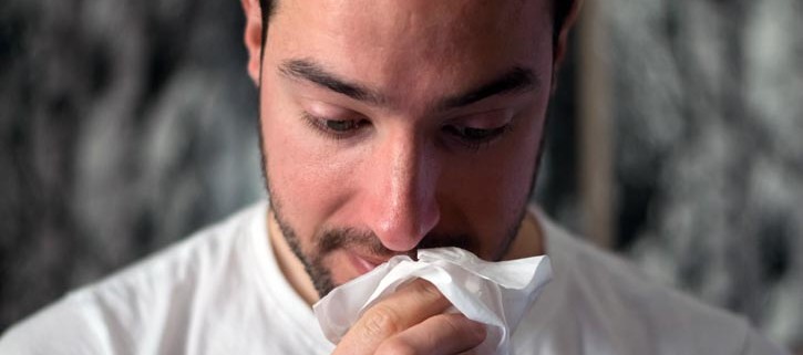 man suffering from allergies and wiping nose
