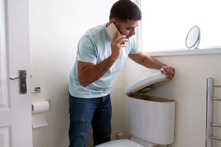 Man lifting toilet tank lid while on the phone