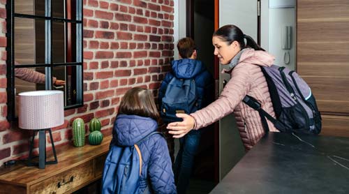 mother and two kids with backpacks and wearing coats leaving home.